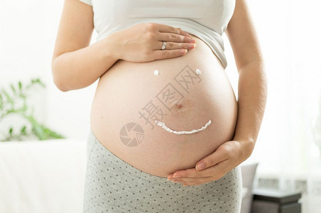 在怀孕的肚子上由creme绘制的微笑标志贴近图像图片