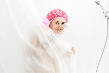 穿着浴帽洗澡和躲在窗帘后面的可爱笑女人肖像图片