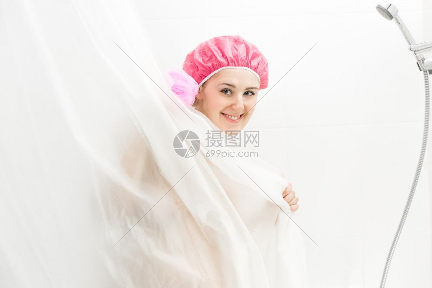 穿着浴帽洗澡和躲在窗帘后面的可爱笑女人肖像图片