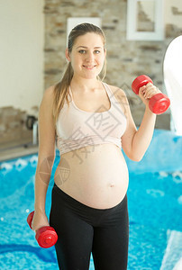 期望婴儿在健身房与哑铃一起运动的妇女图片