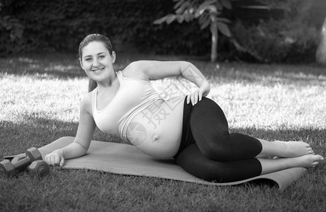 年轻孕妇在做瑜伽前公园草地上伸展的黑白画面高清图片