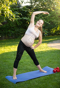 美丽的年轻孕妇在公园绿草地上运动图片