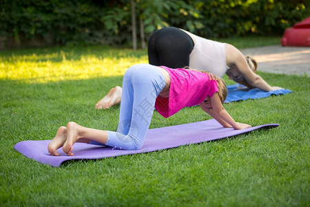 年轻母亲和女儿在草地上做瑜伽图片