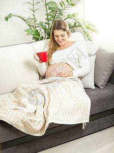 微笑的孕妇在沙发上用茶杯放松图片