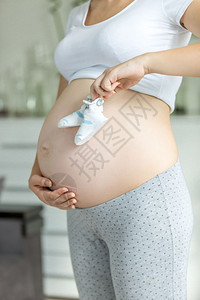年轻孕妇在起居室肚子上冒着婴儿靴的肚上冒着婴儿靴的年轻孕妇图片