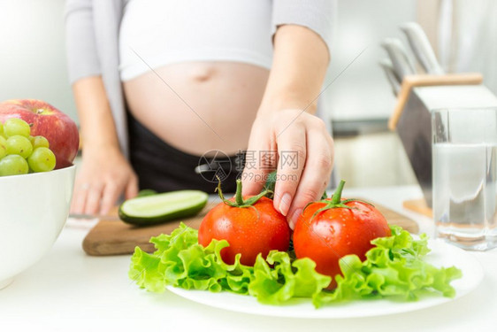 从盘子里抽新鲜番茄的年轻孕妇图片