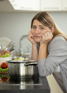 在厨房做饭时坐在桌上的悲伤女人肖像图片