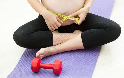 孕妇在健身席上锻炼后用胶带测量腹部图片