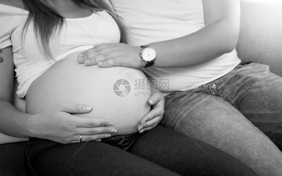 年轻男子用手抓怀孕妻肚的黑白照片图片