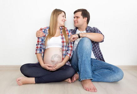 穿牛仔裤的怀孕夫妇和坐在空房间地板上穿衬衫的怀孕夫妇图片