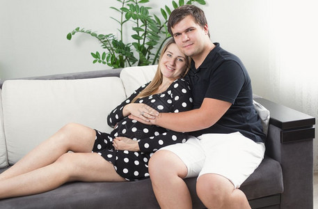 快乐的孕妇和男人在客厅沙发上放松的肖像图片