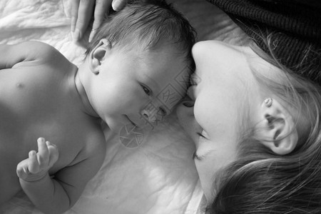 年轻微笑的母亲躺在床上与她一个月大的婴儿躺在床上图片