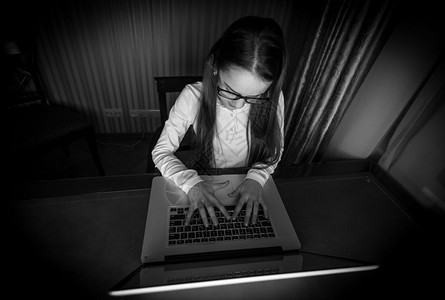 黑白画像少女用笔记本电脑坐在黑暗房间里图片