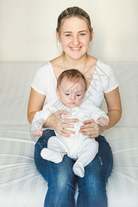 微笑的女人坐在卧室抱着可爱的婴儿在膝上图片