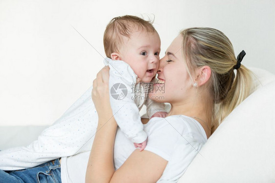快乐的年轻母亲躺在床上抱着她3个月大的婴儿男孩图片