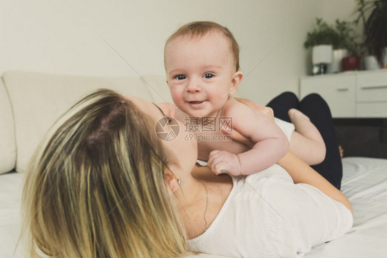 年轻快乐母亲躺在床上抱着婴儿的肖像图片