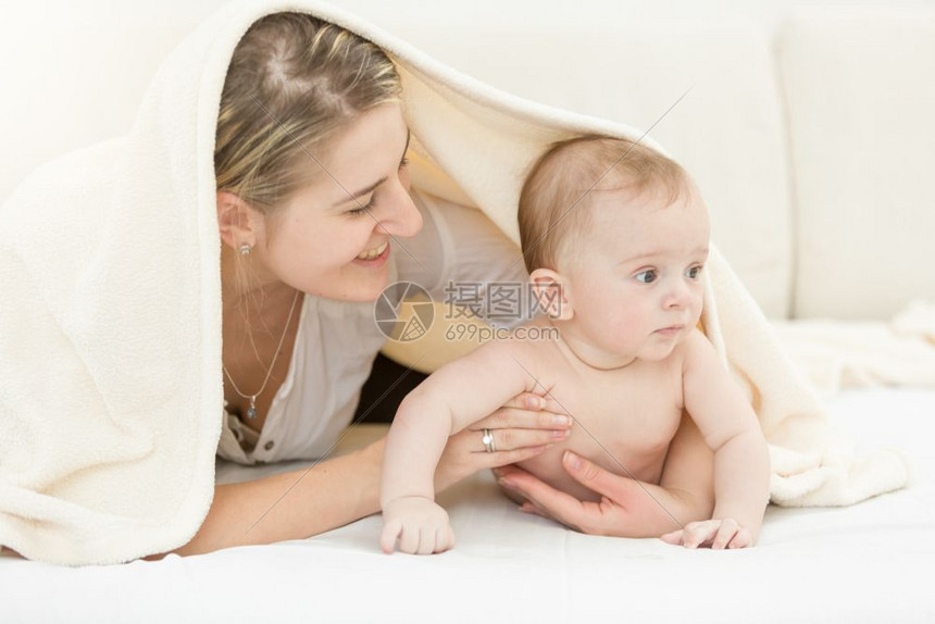 快乐的年轻母亲肖像和她6个月的儿子躺在床上图片