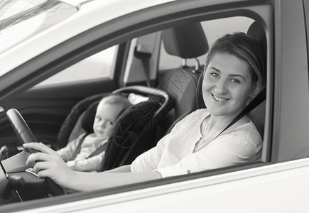 年轻母亲驾驶汽车时婴儿坐在前座的年轻母亲黑白画像图片