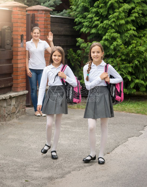 两个笑着的可爱女孩早上带着袋子离开家上学图片
