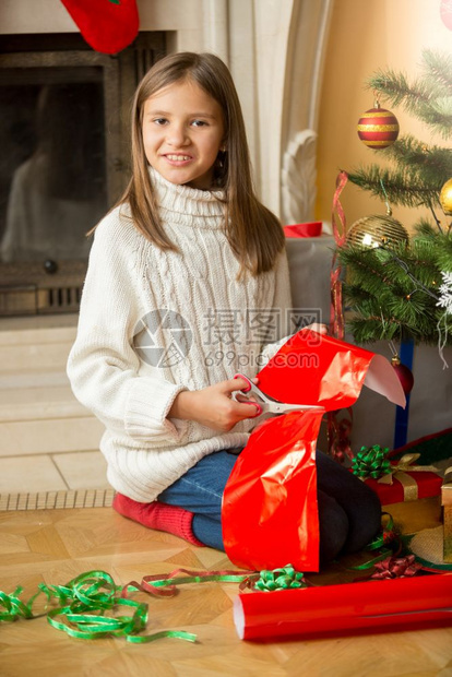 快乐女孩坐在圣诞树上剪红纸包着礼物图片