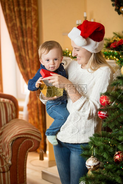 母亲抱10个月大的婴儿和装饰圣诞树的肖像图片