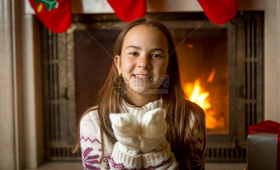 穿着毛衣和手套的快乐笑着女孩在燃烧的壁炉和装饰圣诞树上摆姿势图片