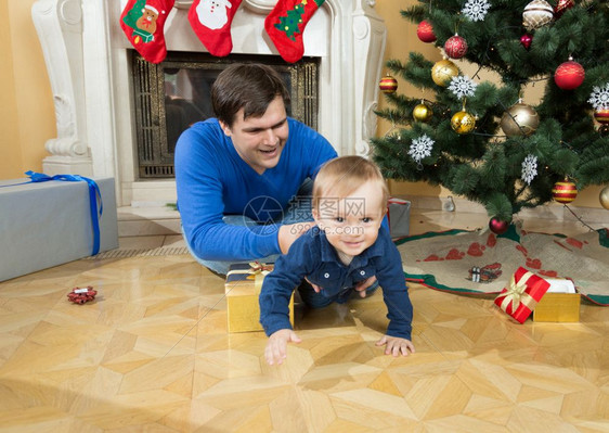 和他儿子在圣诞树下面的地板上玩耍快乐父亲图片