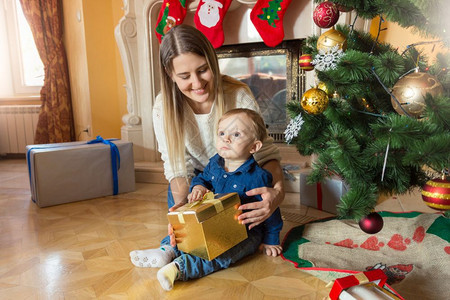 年轻母亲和她的儿女坐在圣诞树上看着礼物盒里背景图片