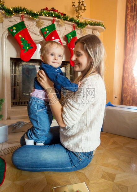 年轻母亲坐在圣诞树的地板上与她男婴同在图片