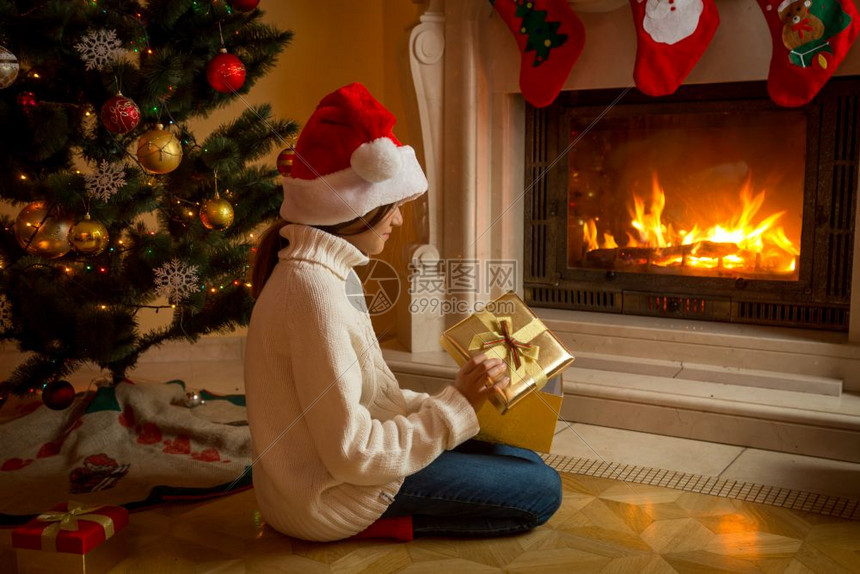 坐在圣诞树旁边的女孩拆礼物图片