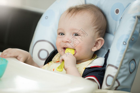 美丽的9个月婴儿男孩在吃饭时用勺子玩图片