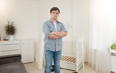 英俊的年轻人站在婴儿床旁图片