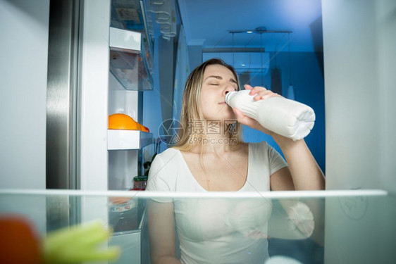 从冰箱里面看晚上喝牛奶的年轻女子图片