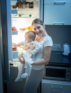 微笑的女人与她儿子一起在夜间厨房的里站着图片