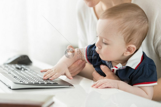 年轻母亲坐在电脑上抱着婴儿在大腿上图片
