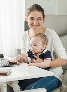 美丽的微笑女士与她儿子一起在电脑上工作图片