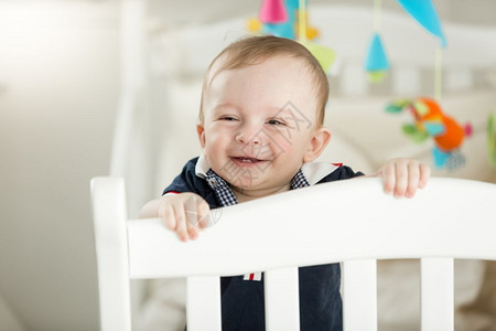 9个月大的微笑婴儿站在白木床上图片
