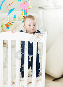 可爱9个月大的男孩站在婴儿床里图片