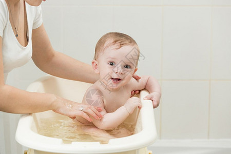 母亲在浴室帮她可爱的婴儿洗澡图片