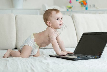 1岁婴儿男孩在尿布中爬伸手拿笔记本电脑图片