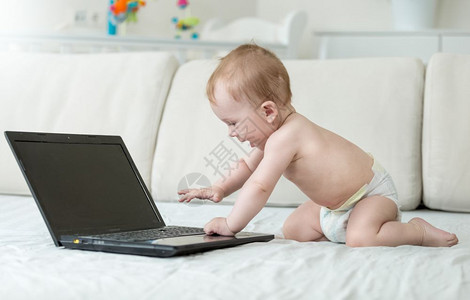 婴儿爬在床上笔记本电脑上感兴趣地寻找图片