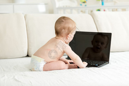 用笔记本电脑坐在床上的婴儿尿布中图片