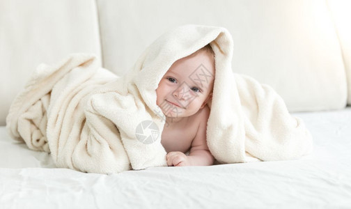 坐在床上盖毯子的可爱婴儿男孩图片