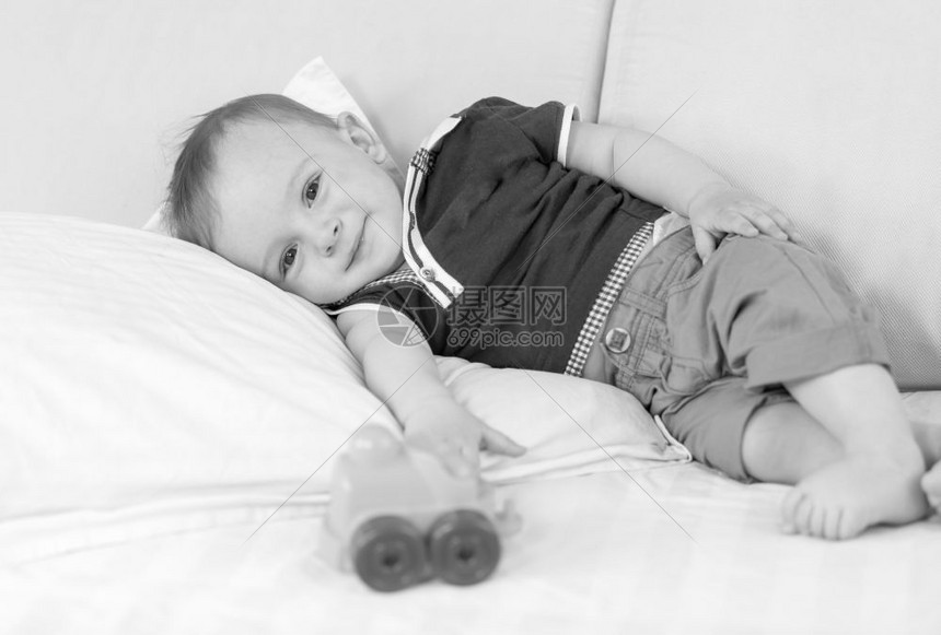 1岁男孩玩具后躺在床上的黑白画面图片