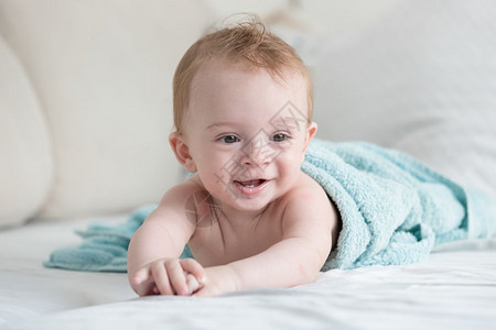 淋浴后躺在床上蓝毛巾中微笑的婴儿肖像图片