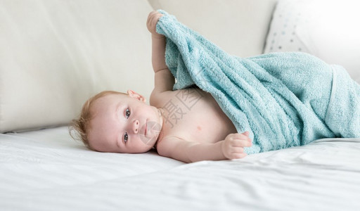 9个月大的婴儿男孩坐在毛巾下面的床上图片