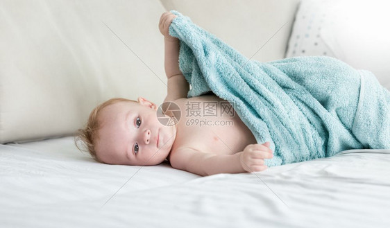 9个月大的婴儿男孩坐在毛巾下面的床上图片