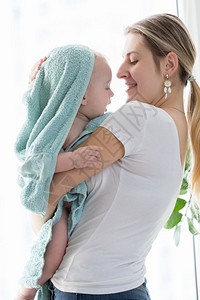 快乐的年轻母亲抱她的孩子男浴后裹着蓝毛巾图片