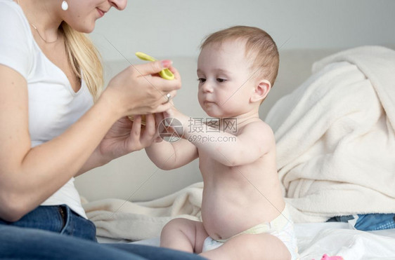 母亲给坐在床上的女婴儿子倒汤图片