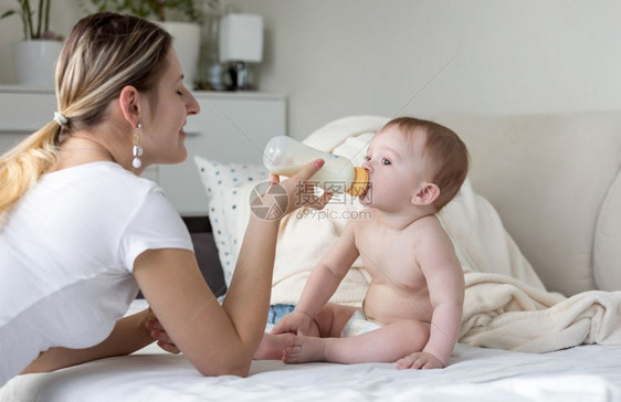 婴儿男孩坐在床上喝牛奶的肖像图片